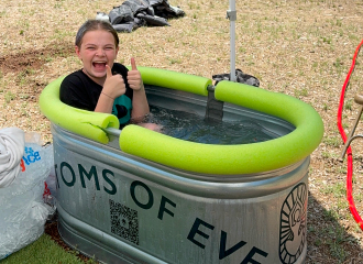 Youth sitting in an aluminum farm basin filled with water and lined with a bright green pool noodle