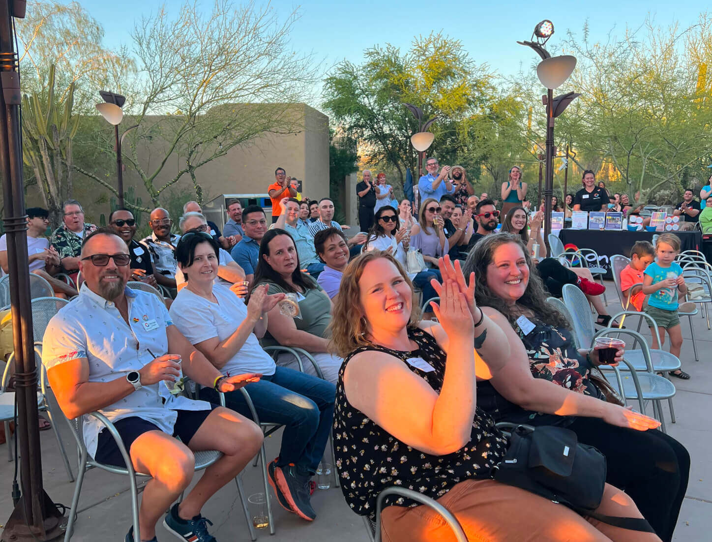 Group of people applauding at an outdoor fundraiser taking place in the evening during sunset