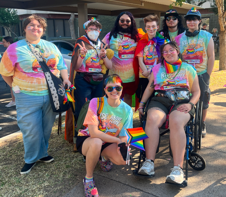 group of people dressed in rainbow tie-dyed shirts posing for the camera outside an apartment complex