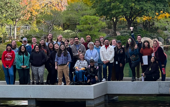 A group of one•n•ten employees posing on a cement bridge that appears to be floating in a small lake