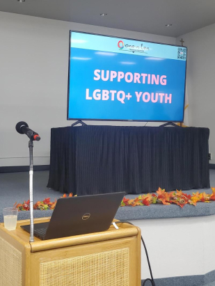 Podium and large tv on a black tablecloth draped table that says, "Supporting LGBTQ+ Youth"