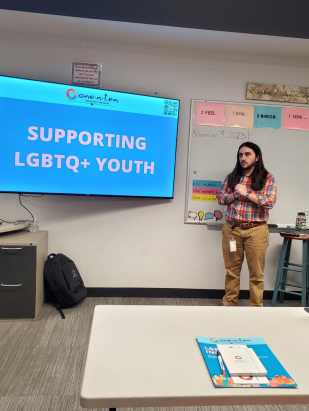 Gentleman with long, dark hair standing at the front of a classroom delivering a presentation