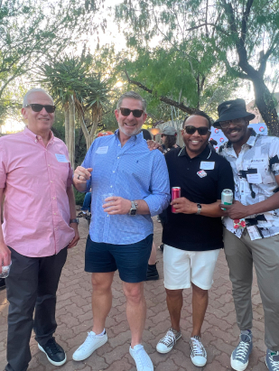 Four adult men of different ethnic backgrounds standing under trees at a LGBTQ fundraising event