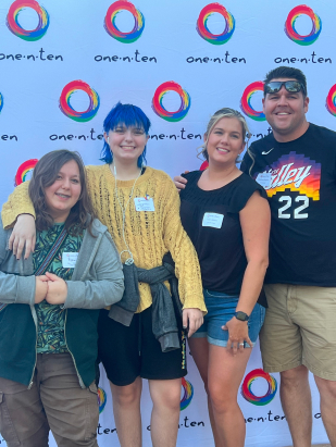 An LGBTQ family standing in front of a branded backdrop at a fundraising event