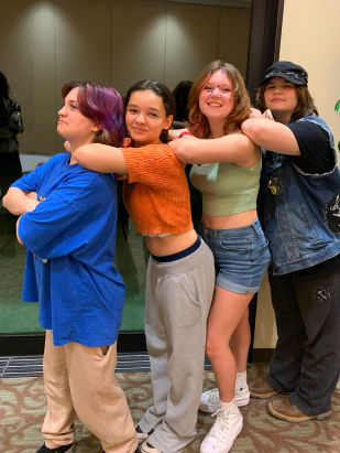 Group of four teens standing in a row with their elbows leaning on the shoulders of the person in front of them