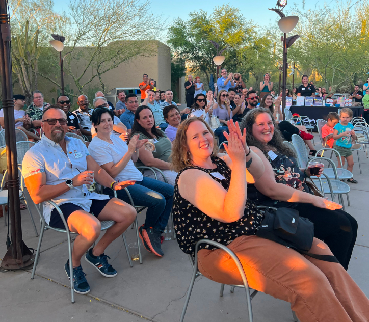 Group of people applauding at an outdoor fundraiser taking place in the evening during sunset