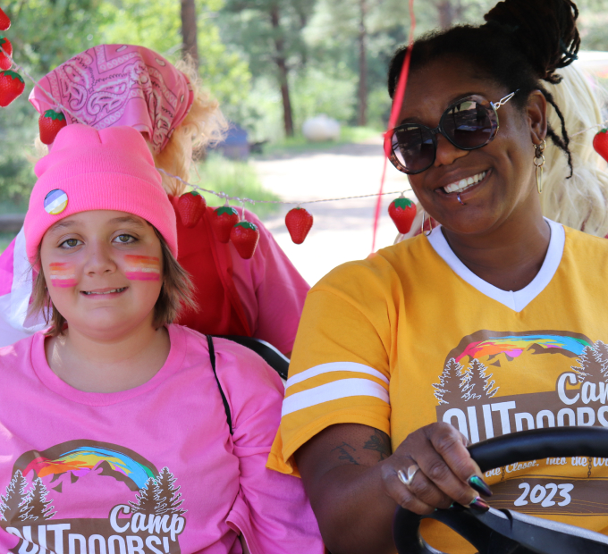 A young girl in a pink shirt and a black young adult in a yellow shirt smiling