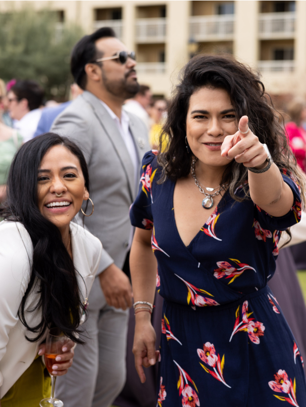 Hispanic woman with long, wavy hair wearing a dress pointing at the camera