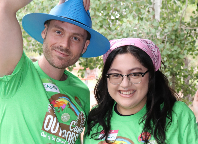 A male and female wearing matching green Camp Outdoors t-shirts