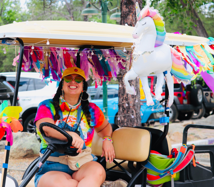 Happy adult female sitting on a decorated golf cart adorned with rainbow streamers and an inflatable unicorn