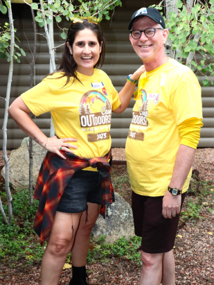 Two parents standing together in the woods, infront of a cabin during Camp Outdoors