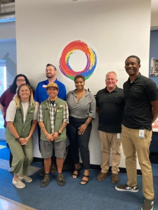 Group of one•n•ten staff standing in front of a wall with the organization's logo on it.