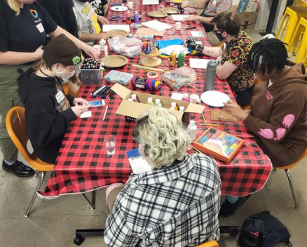 group of youth sitting around a large table covered in a red and black table cloth doing arts and crafts