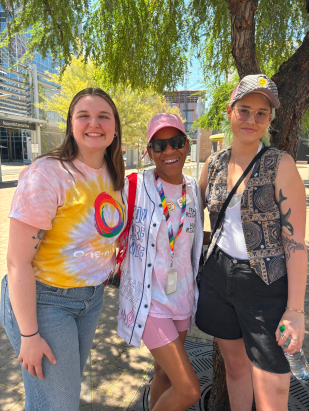 three girls standing together outside under a tree and smiling