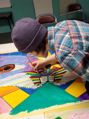 Asian youth wearing a beanie leaning over a painting they are working on