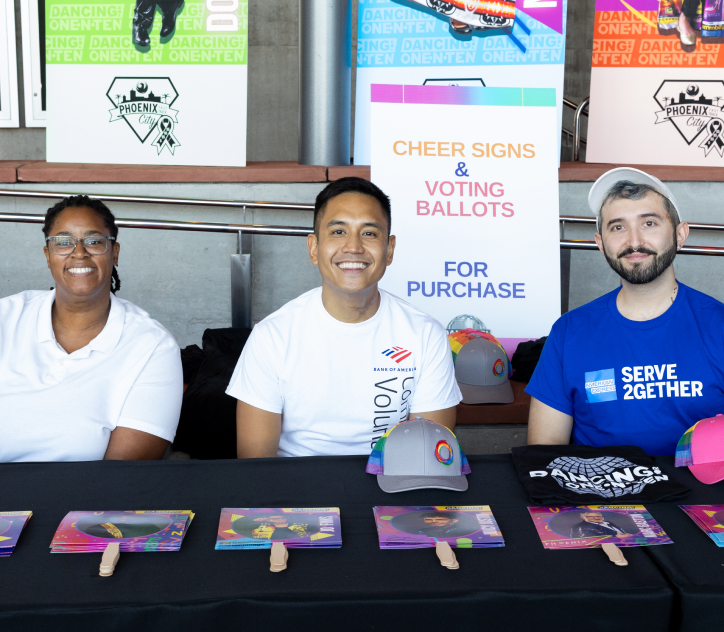 Three adult volunteers of diverse ethnic backgrounds sitting at a table waiting to greet event attendees