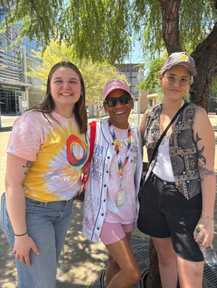 three girls standing together outside under a tree and smiling