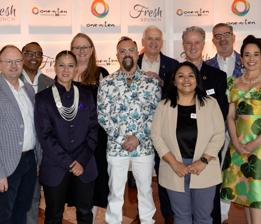 A group of professional adults dressed nicely and standing in front of a branded, back-lit backdrop