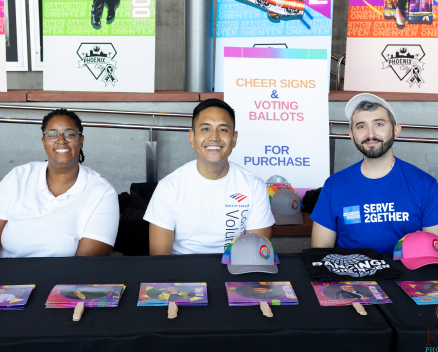 Three adults of diverse backgrounds sitting at a table to greet event attendees