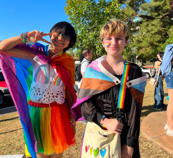 two young people dressed in rainbow clothes smiling outside