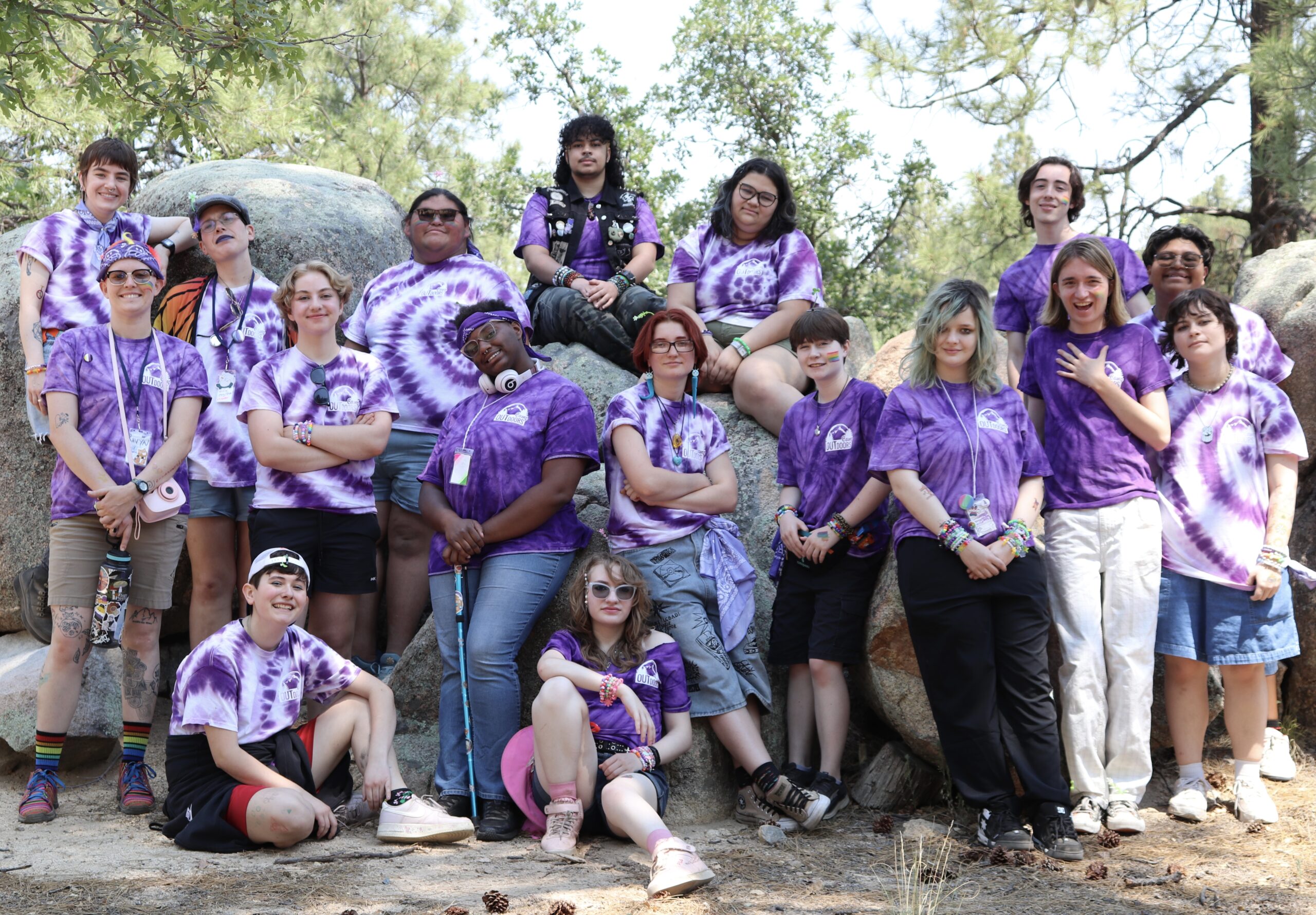 Group of camp outdoors attendees wearing purple tie dyed Camp Outdoors shirts posing on rocks with their cabin mates